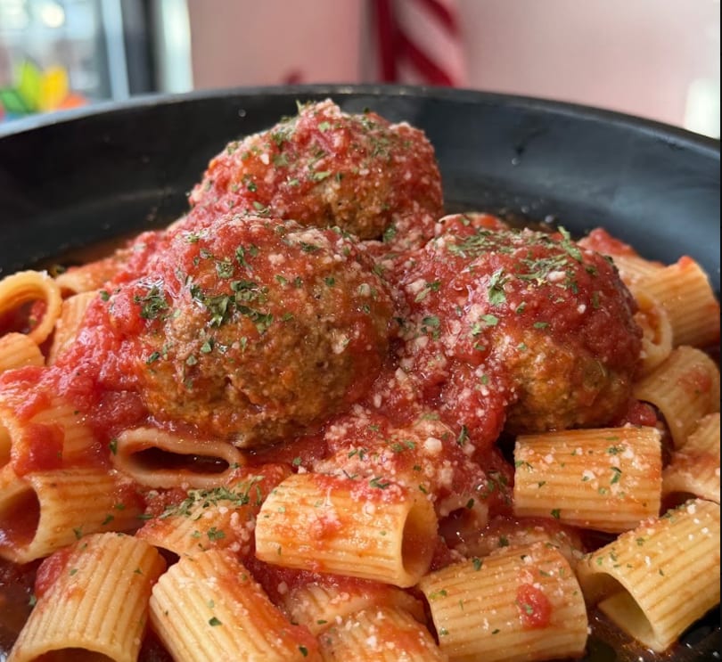 Rigatoni pasta with three large meatballs, red sauce, grated cheese, and parsley in a black bowl.