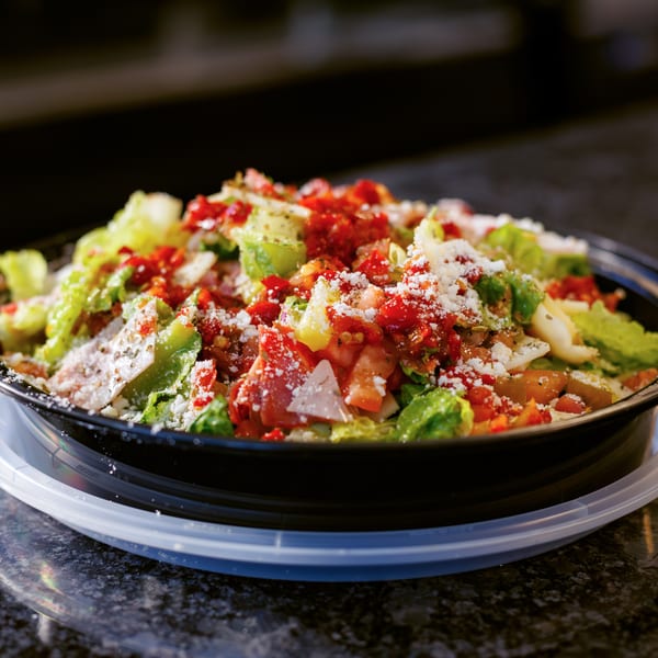 Fresh salad with lettuce, diced tomatoes, and grated cheese in a black bowl on a dark counter.