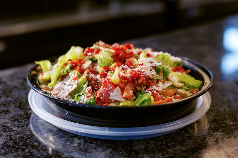 Fresh salad with lettuce, diced tomatoes, and grated cheese in a black bowl on a dark counter.