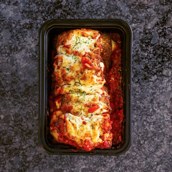 Baked lasagna with melted cheese, tomato sauce, and herbs in a black rectangular container.